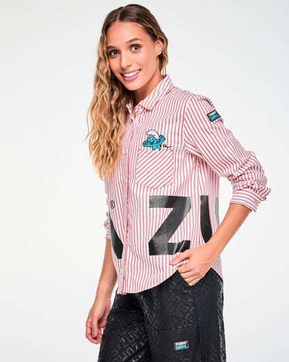 Female model in the red and white striped button-up with sleeves pushed up, shown in side view with the black 'ZUMBA' letters continuing around her left side, a black 'ZUMBA' X 'THE SMURFS' patch on the left sleeve, and the embroidered Smurf above the left chest pocket.