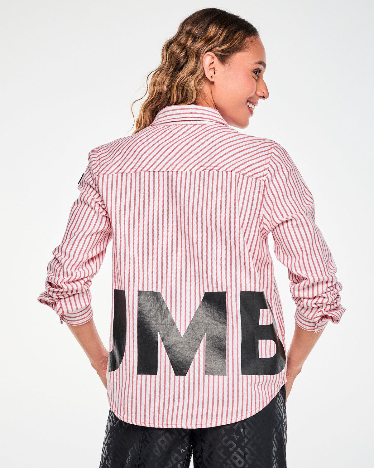 Shown from the back, a female model in the red and white striped shirt, with part of the large black ‘ZUMBA’ lettering wrapping across the lower back and diagonal stripes on the shoulder yoke.