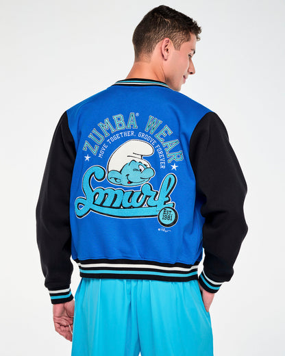 Shown from the back, a male model in the blue and black varsity jacket, with the 'ZUMBA WEAR' and 'Smurf' back graphic framed by the black sleeves and the striped ribbed hem. Paired with aqua blue cargo pants.