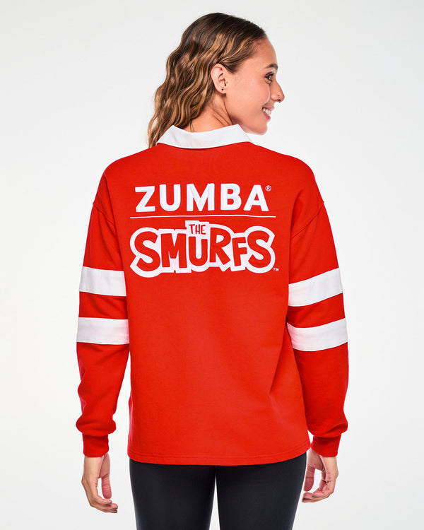Back view of a female model in the red rugby polo, with embroidered white 'ZUMBA' text over a thin line and a white-outlined 'THE SMURFS' logo across the upper back.