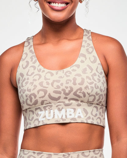 Close-up of a beige longline scoop neck bra with an all-over light brown leopard print and white 'ZUMBA' text across the wide underband.