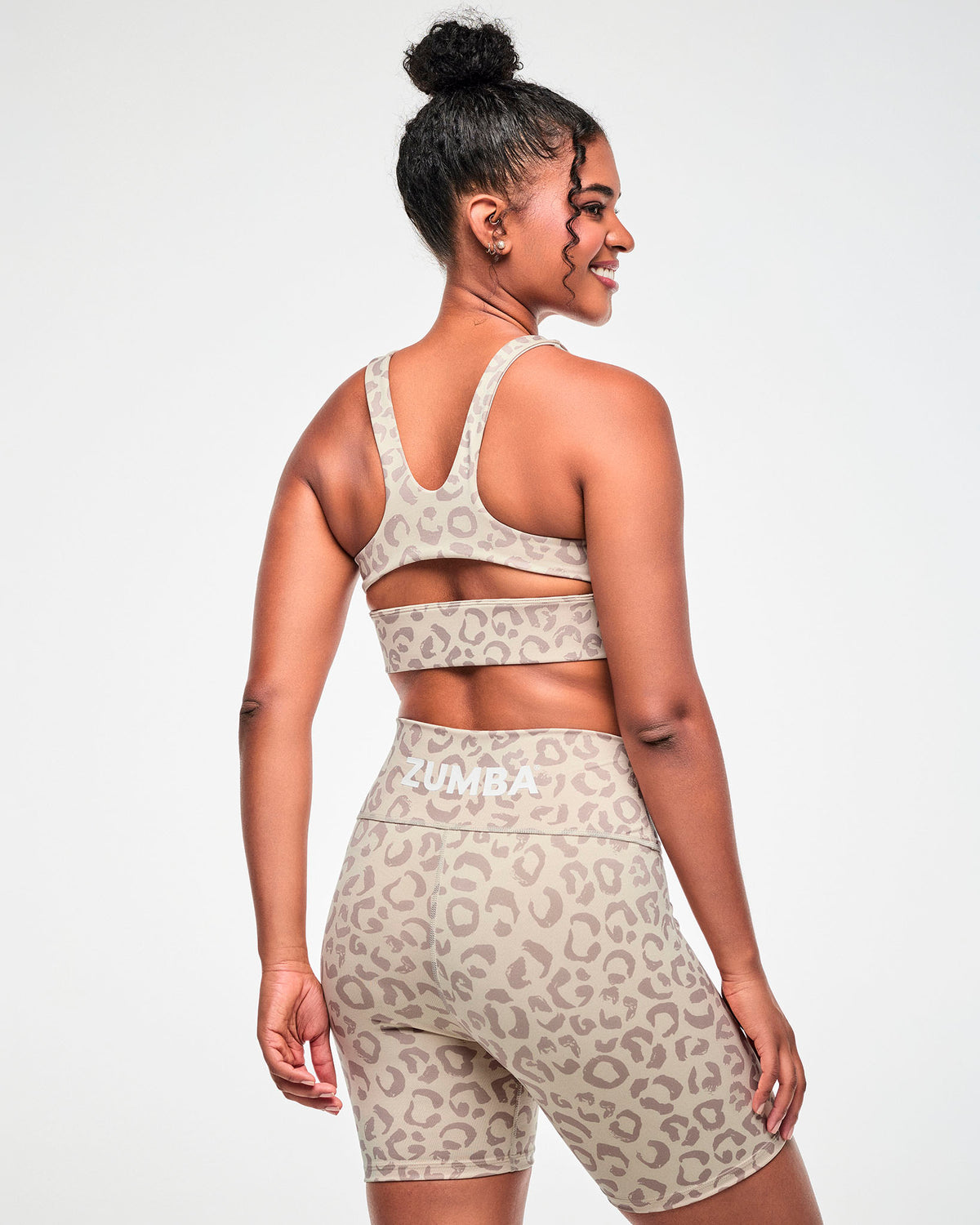 Shown from the back, a female model wears the beige leopard print racerback bra with a keyhole cutout, paired with matching biker shorts.