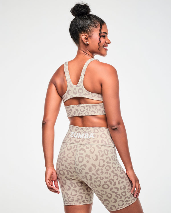 Shown from the back, a female model wears the beige leopard print racerback bra with a keyhole cutout, paired with matching biker shorts.