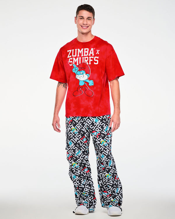 Male model in the oversized red and light cloud fabric wash tee with white 'ZUMBA' X 'THE SMURFS' text and the pointing Papa Smurf graphic, paired with black and white Smurfs print cargo pants.