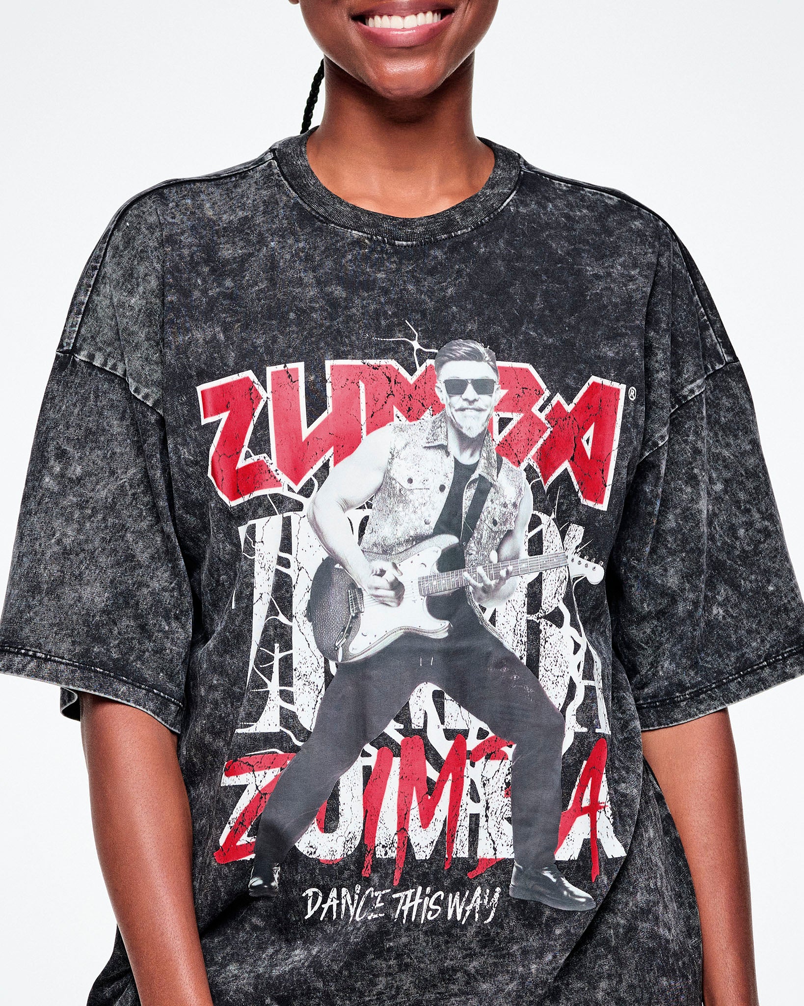 Close-up of the black acid-wash graphic tee with Beto, the creator of Zumba, smiling in sunglasses jamming on a guitar in black and white with ZUMBA in red and white text behind him and Dance this Way in smaller white text underneath.
