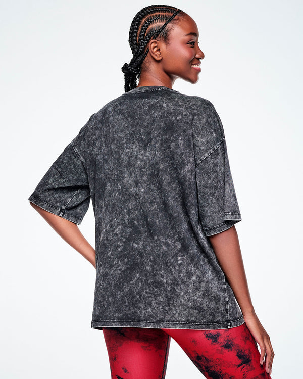 Back view of a female model wearing a black acid-wash graphic tee, paired with red and black leggings.