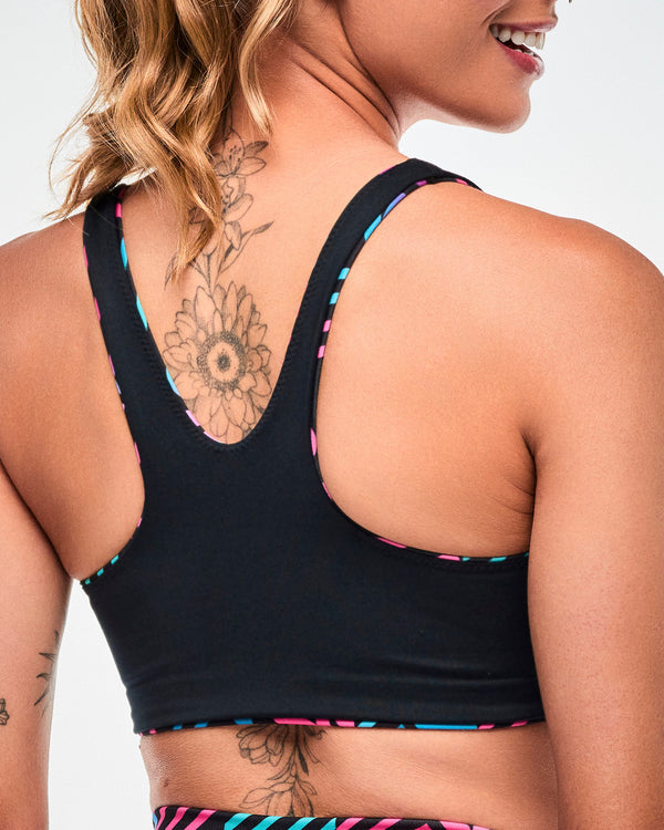 Shown from the back, close-up of the reversible bra, in black, with striped aqua and pink trim along the edges.