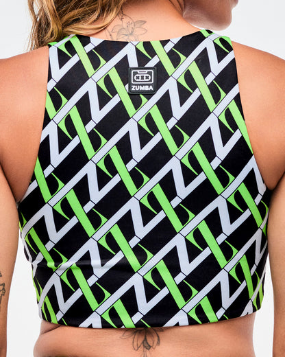 Back view of a female model wearing black based crop top with an allover white and green “Z” crisscross pattern with a black and white Zumba patch on the top.