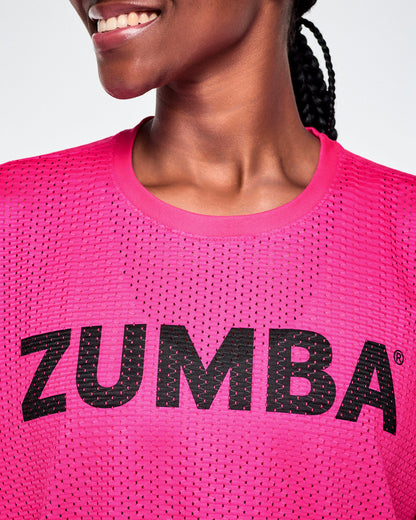 Close-up of a female model wearing a bright pink Zumba mesh top with a black ZUMBA lettering across the chest.