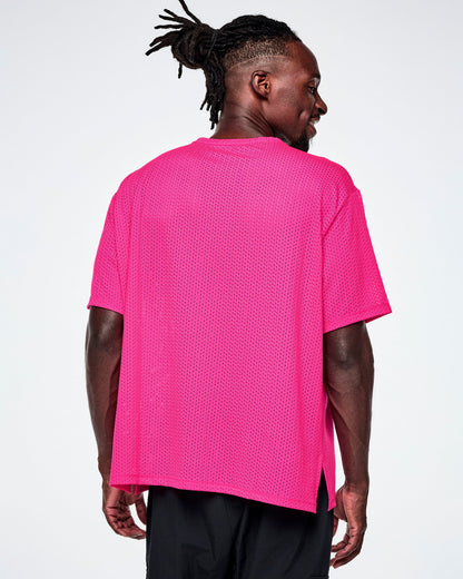 Back view of a male model wearing a neon pink oversized mesh boxy top, paired with black pants against a white background.