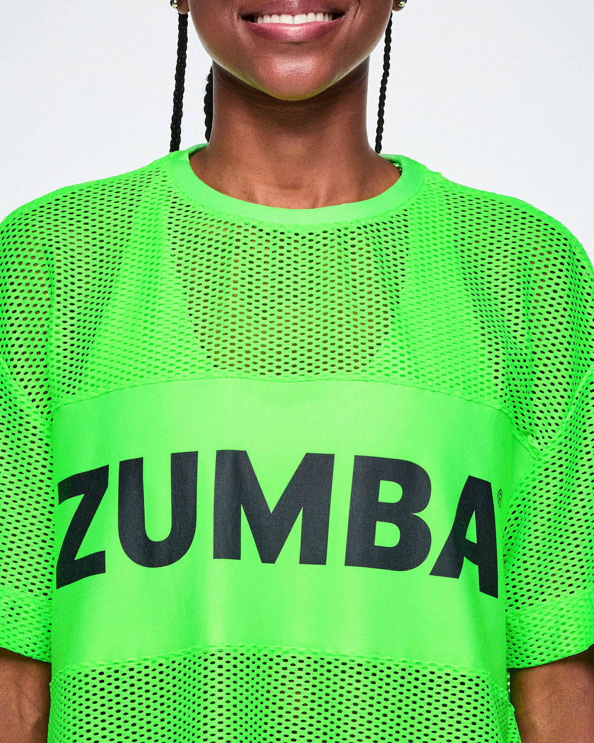 Close-up of a female model wearing a bright green Zumba mesh top with a large black ZUMBA letters across the chest.