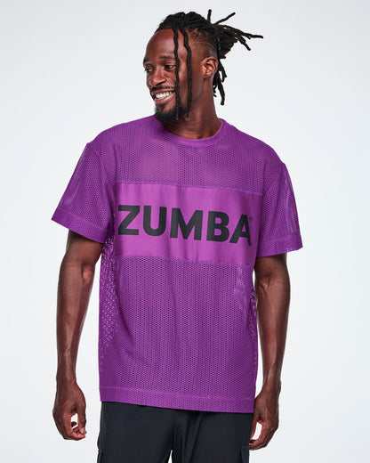 A male model wearing a purple Zumba mesh top with a wide band across the chest featuring the black ZUMBA text, paired with black pants.