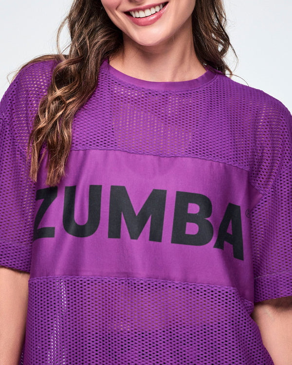 Close-up of a female model wearing a purple Zumba mesh top with a large black ZUMBA letters across the chest.