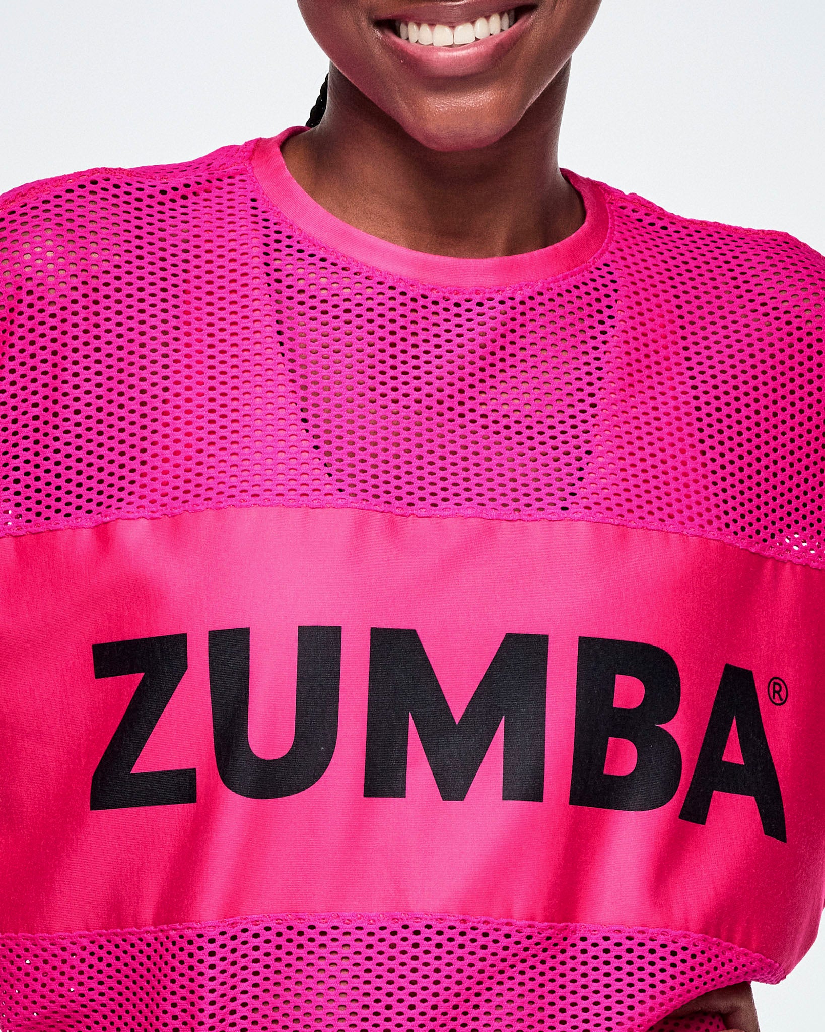 Close-up of a female model wearing a bright pink Zumba mesh top with a large black ZUMBA letters across the chest.