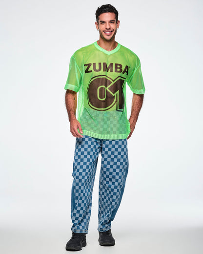 Full view of a male model wearing a green mesh Zumba tee with a large black “ZUMBA 01” on the front, paired with blue checkered denim pants and black shoes.