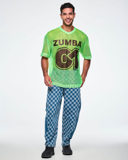 Full view of a male model wearing a green mesh Zumba tee with a large black “ZUMBA 01” on the front, paired with blue checkered denim pants and black shoes.