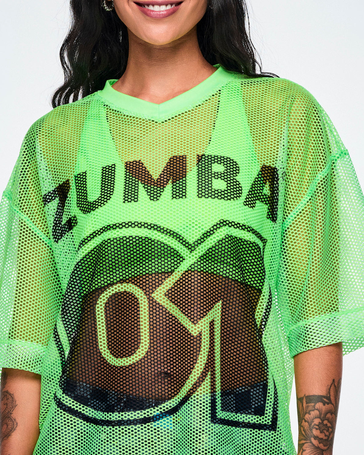 Close-up detail of a female model wearing a green mesh Zumba top, with a large black "ZUMBA 01" printed on the front.