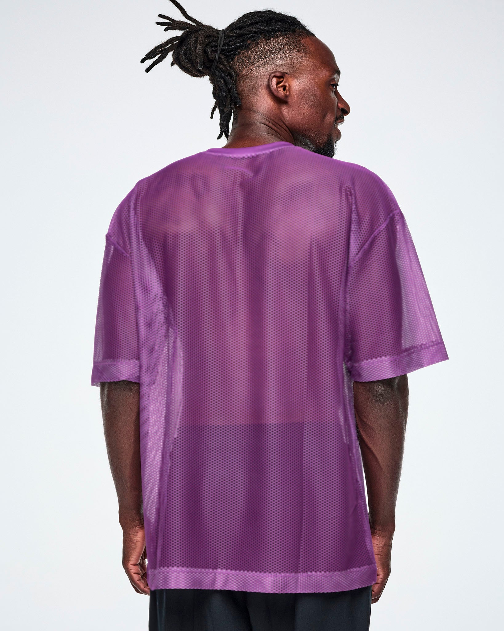 Back view of a male model wearing a purple mesh Zumba top with a large black "ZUMBA 01" printed on the front, paired with black pants.