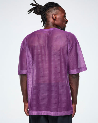 Back view of a male model wearing a purple mesh Zumba top with a large black "ZUMBA 01" printed on the front, paired with black pants.