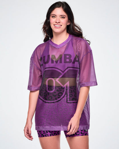 A female model wearing a purple mesh Zumba top with a large black "ZUMBA 01" printed on the front, paired with purple leopard print high-waisted biker shorts.