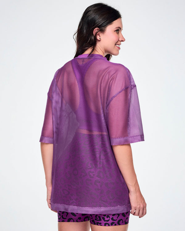 Back view of a female model wearing a purple mesh Zumba top with a large black 