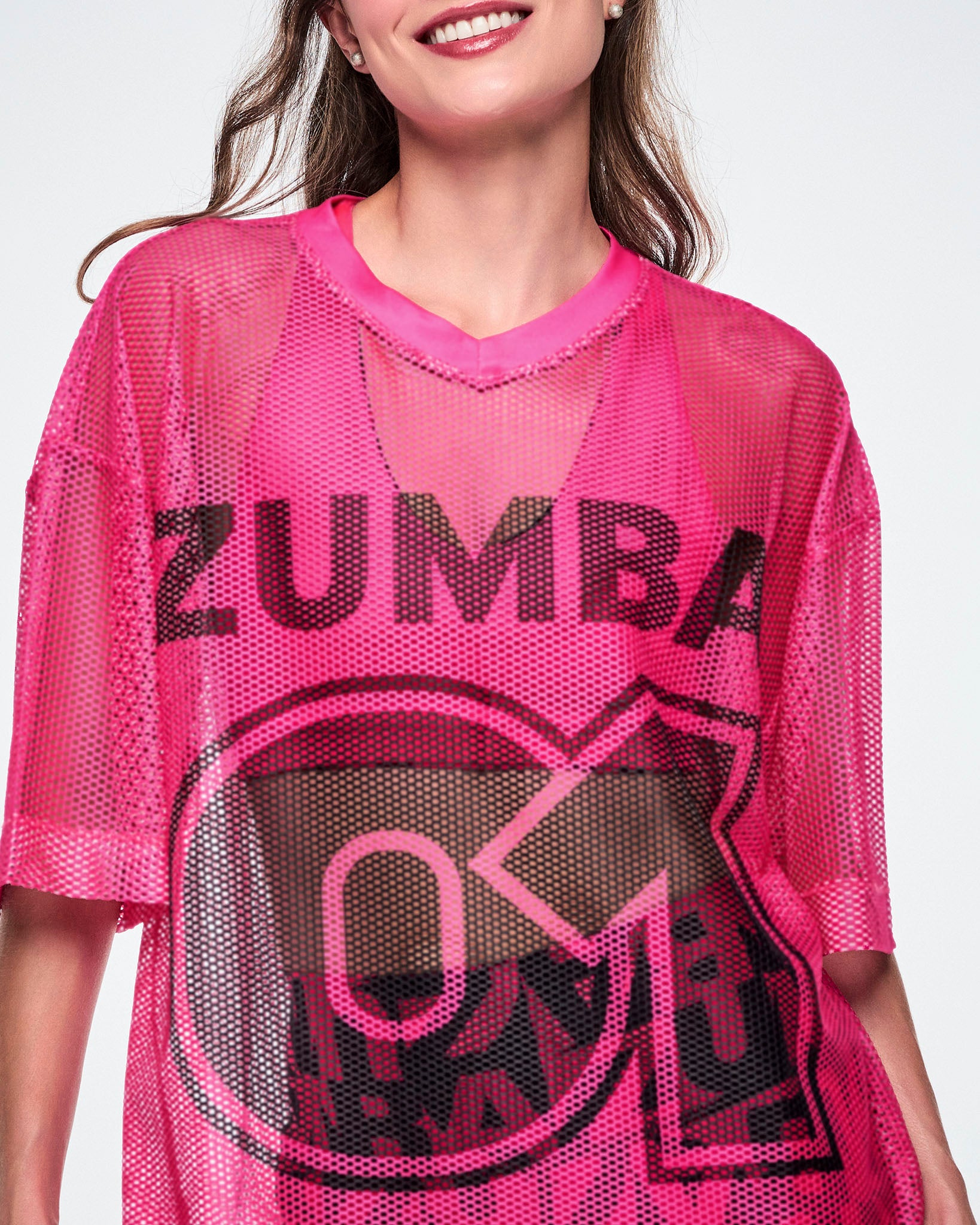 Close-up detail of a female model wearing a pink mesh Zumba top, with a large black "ZUMBA 01" printed on the front.