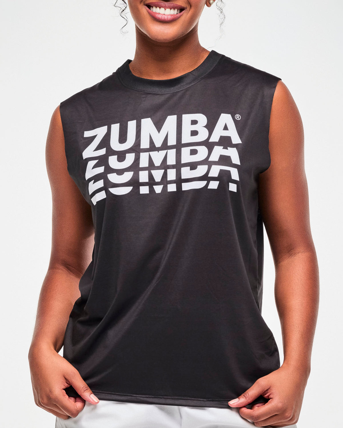 Close-up of the black sleeveless muscle tee's stacked white 'ZUMBA' print, female model.