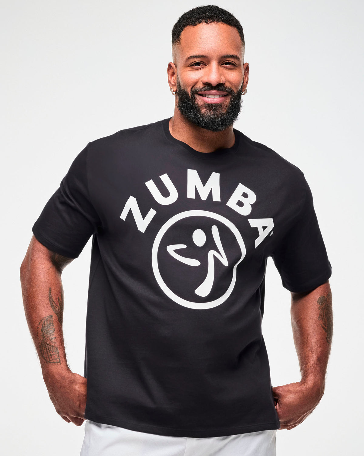 Male model in the black oversized T-shirt with white 'ZUMBA' text and a Zumbito logo, paired with white pants.