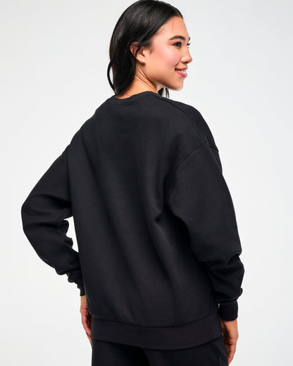 Shown from the back, the black waffle-knit crewneck sweatshirt on a female model, highlighting the oversized silhouette.