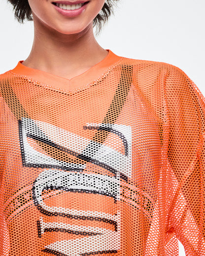 Female model close-up of the orange mesh shirt with silver Zumba lettering. 