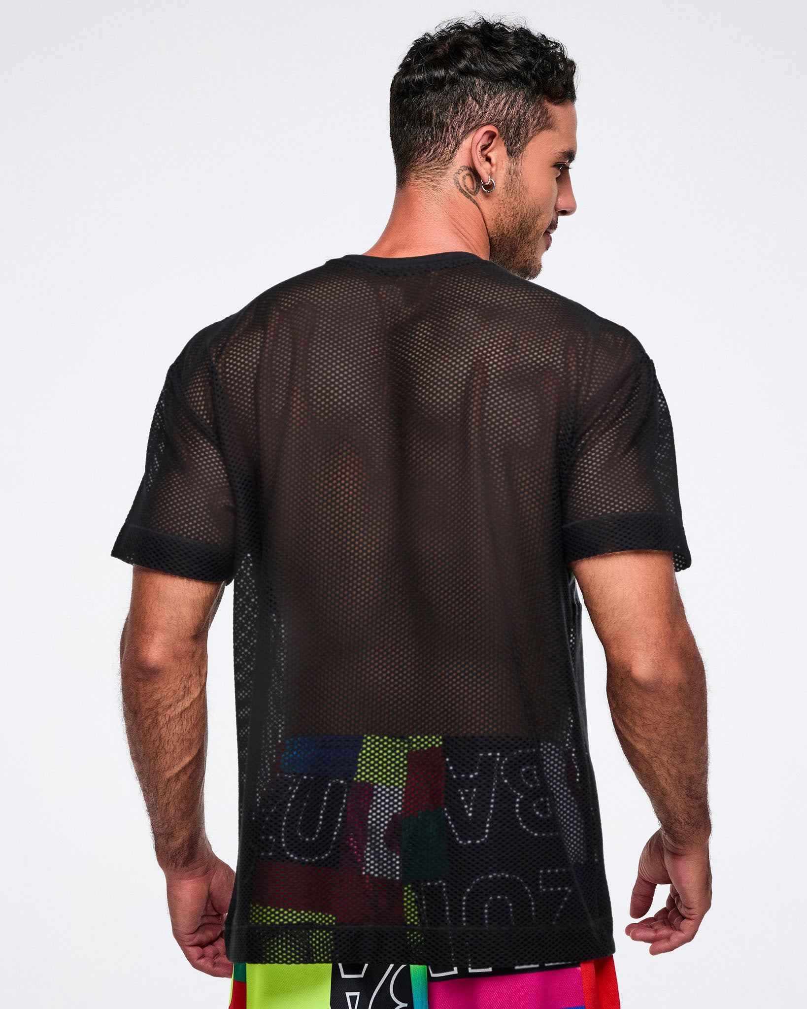 Back view of a male model wearing a black Zumba mesh shirt with colorful letters on a plain background.