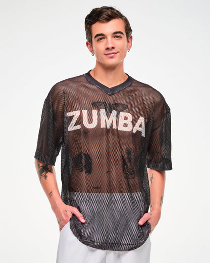 Male model in the black mesh oversized top with white 'ZUMBA' text, both hands in the pockets of white pants.