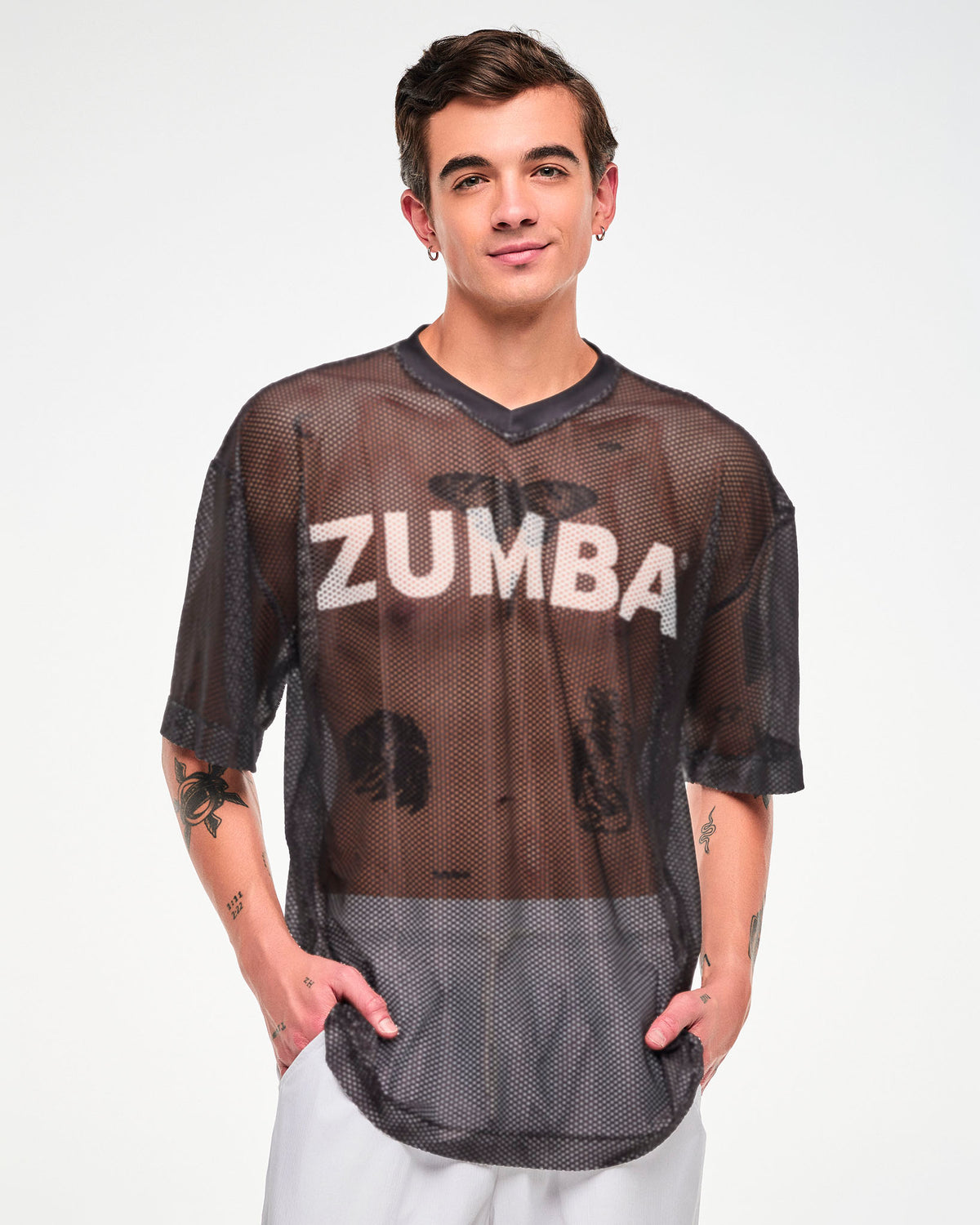 Male model in the black mesh oversized top with white 'ZUMBA' text, both hands in the pockets of white pants.