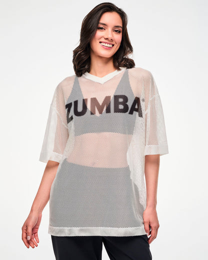 Female model wearing the white mesh oversized top with black 'ZUMBA' text, smiling.