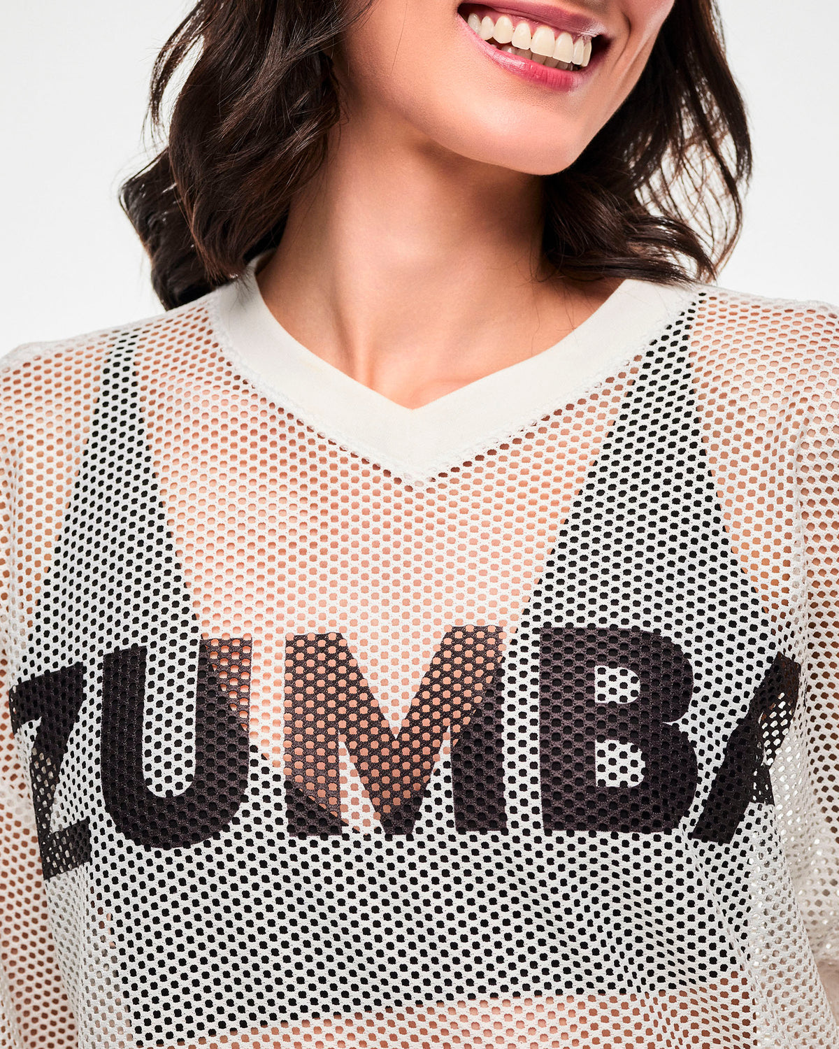 Close-up of the white mesh, the black 'ZUMBA' text near the V-neckline, female model.