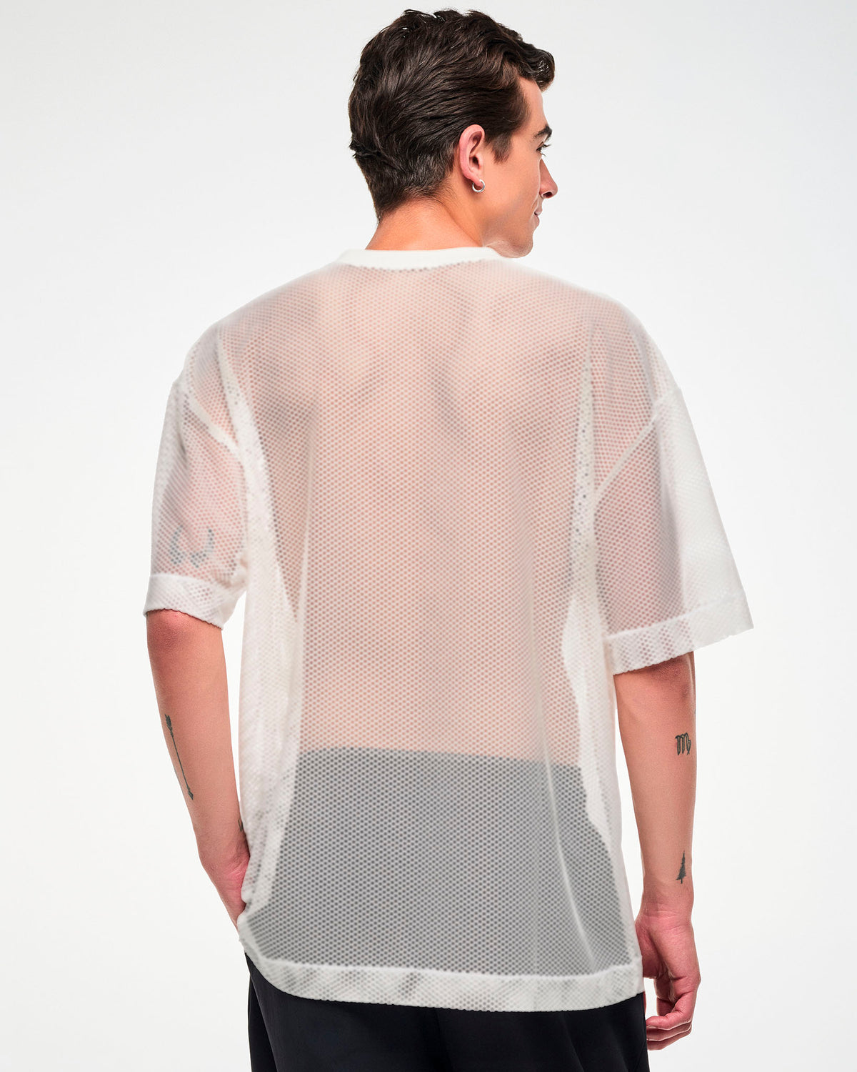 Back view of the white mesh oversized top, male model, showing the sheer fabric and dropped hem.