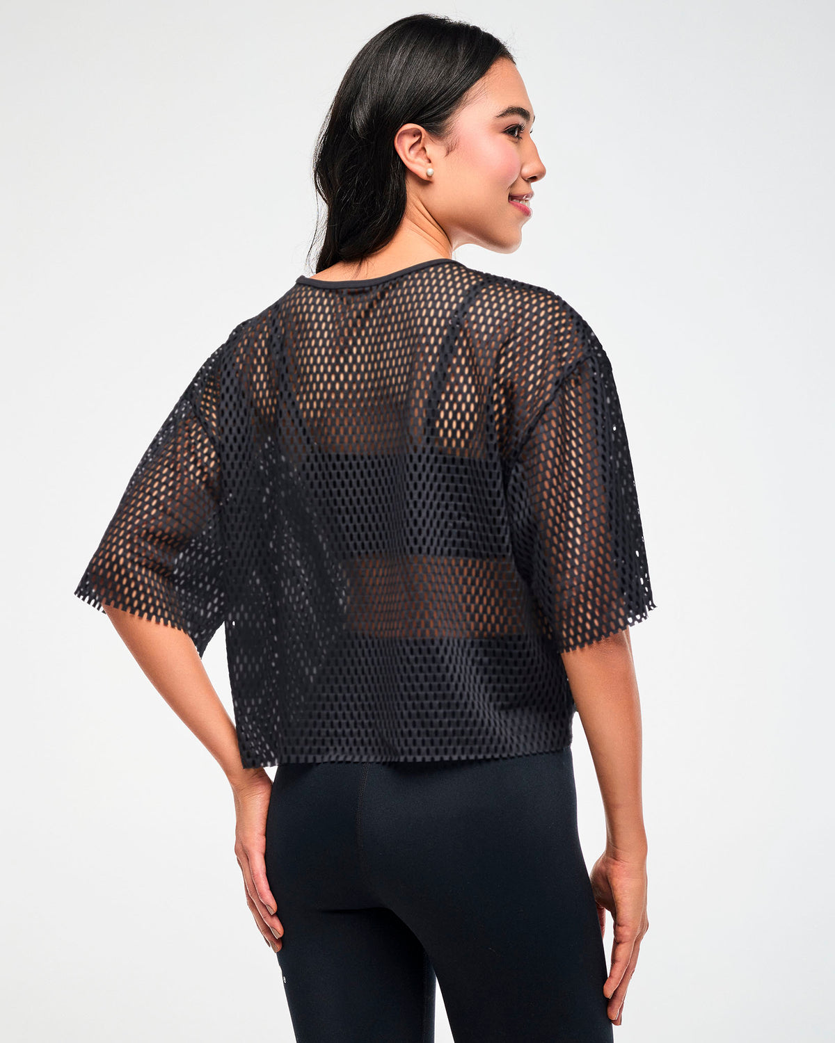 Back view of the black mesh cropped top, female model, paired with black leggings.