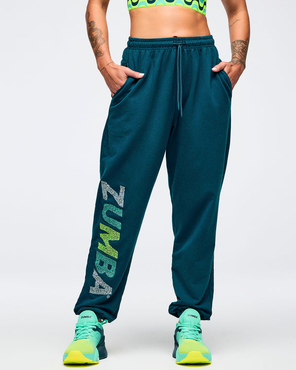 Teal jogger sweatpants with elastic drawstring waistband and relaxed tapered fit, modeled by a female wearing ombre green to lime athletic sneakers on a white studio background.