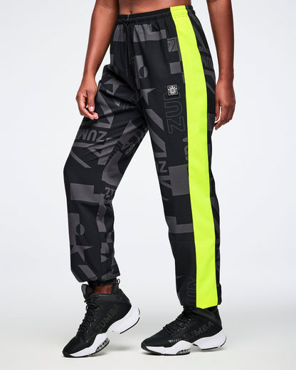Left side view of a male model wearing black and gray patterned pants with neon yellow stripe down the leg on a white background.
