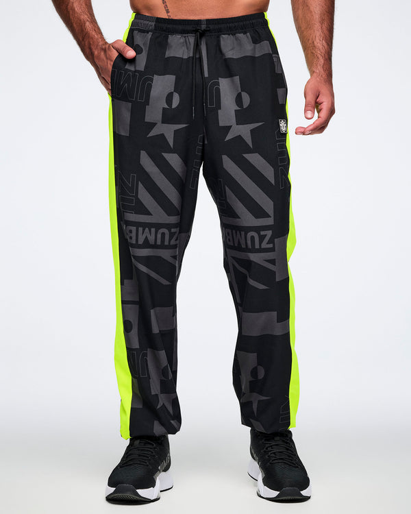 Male model with his right hand in a pocket, wearing black and gray patterned pants with neon yellow stripes on both legs on a white background.