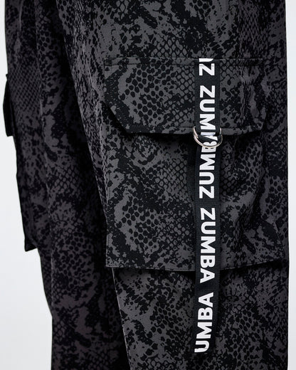 Close-up of black and grey snakeskin-patterned cargo pants with a vertical black strap on the cargo pocket with white 'ZUMBA' text.