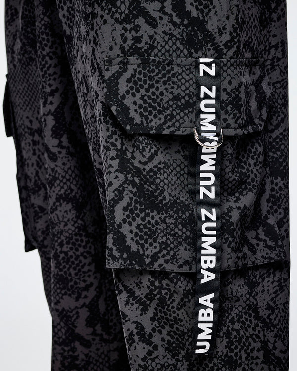 Close-up of black and grey snakeskin-patterned cargo pants with a vertical black strap on the cargo pocket with white 'ZUMBA' text.