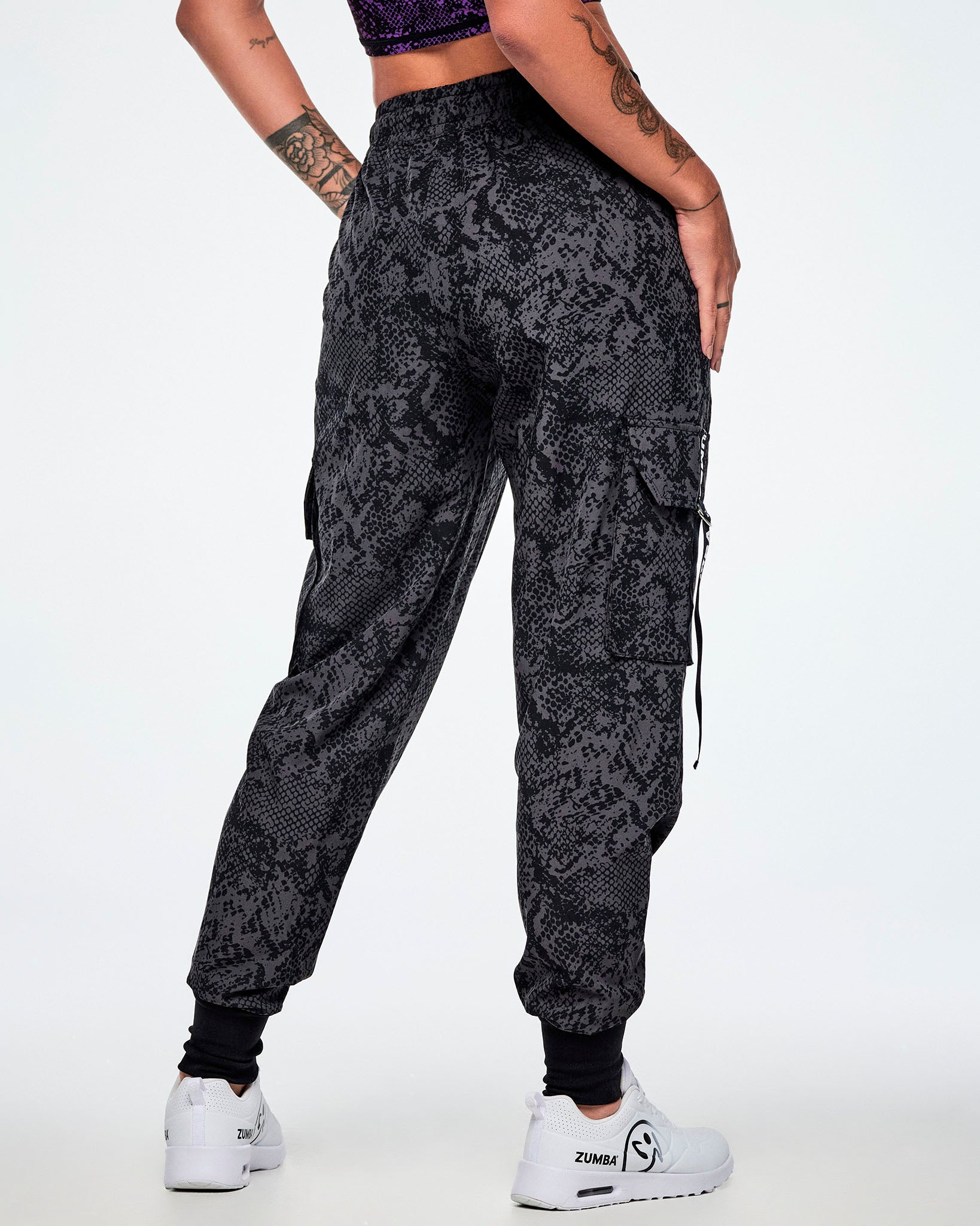 Back view of a female model wearing black and grey snake-skin patterned cargo pants and paired with white shoes.