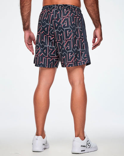 Back view of a male model wearing mesh shorts featuring a bold black, white, and red ZUMBA text pattern, a black stripe down the side and paired with white shoes.