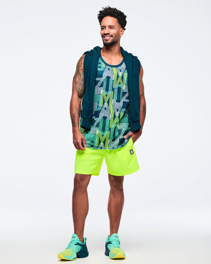 Teal, navy, and lime graphic-print mesh tank top styled with neon lime shorts and a teal sweatshirt draped over the shoulders, modeled by a male wearing teal-to-lime athletic sneakers on a white studio background.
