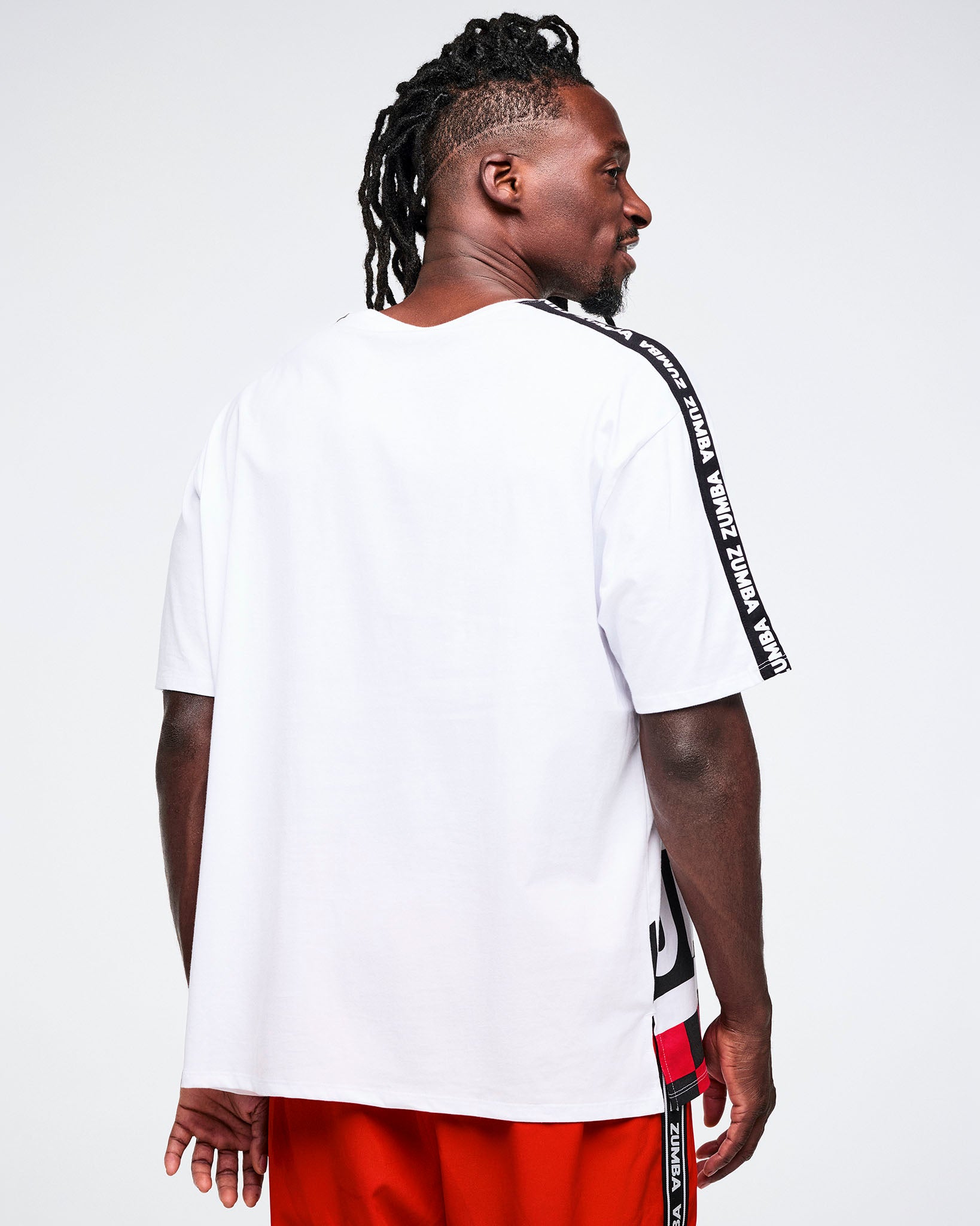 Male model from behind, wearing a white t-shirt with black text on sleeves and red pants against a white background.