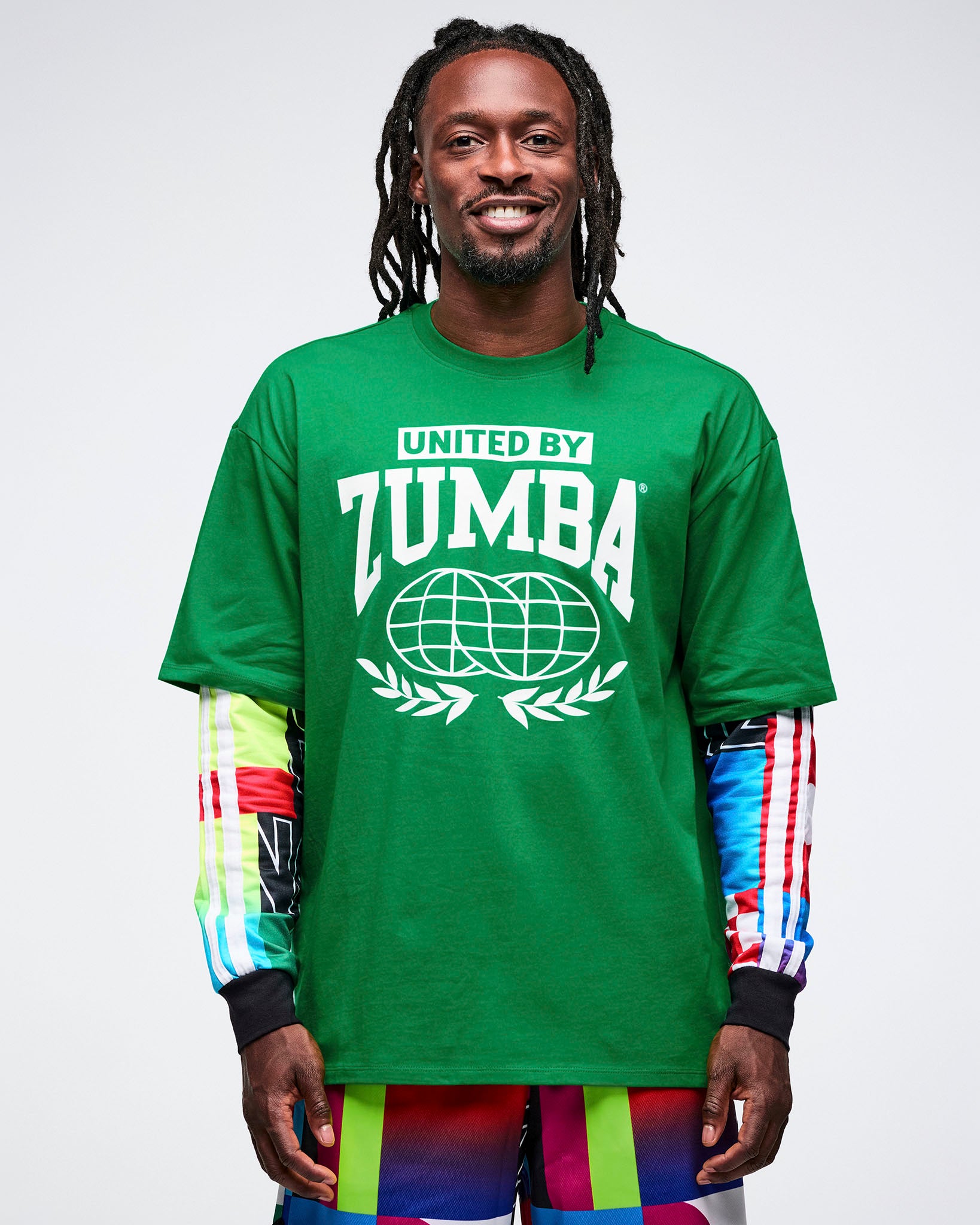 Male model wearing a green Zumba t-shirt over a shirt with colorful sleeves on a white background.