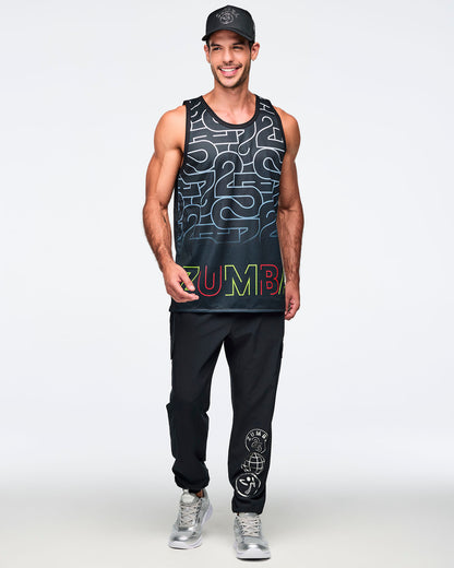 Black mesh tank with an allover silver 25 graphic and multicolor Zumba logo at the hem. A smiling male model wears the sleeveless longline tank with black jogger pants, with silver graphics on the left leg, silver sneakers, and a black baseball cap against a light gray background.