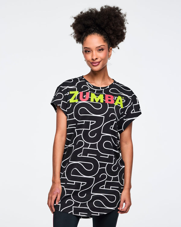 Black, long, round hem tee with an allover white 25 graphic and multicolor Zumba logo across the chest. A female model wears the short-sleeve, round hem tee over black leggings against a light gray background.