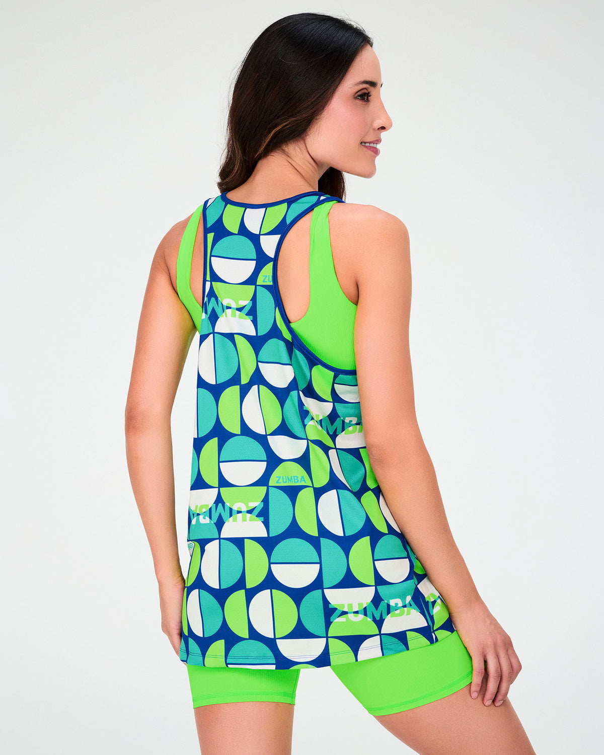 Back view of a female model in the dark blue half-circle print racerback tank, a neon green bra visible at the sides, with neon green biker shorts.